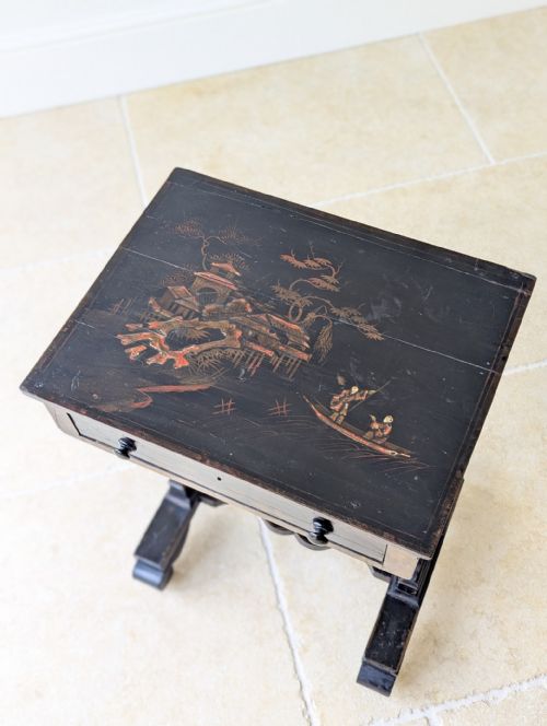 fig 1. An antique Regency ebonised work table featuring Chinoiserie artwork on the rectangular top, a single drawer, and trestle support legs.