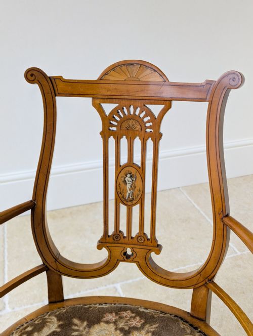 fig 1. An antique satinwood armchair featuring a carved lyre-shaped backrest with marquetry inlay, turned arms and legs, and a floral upholstered seat.