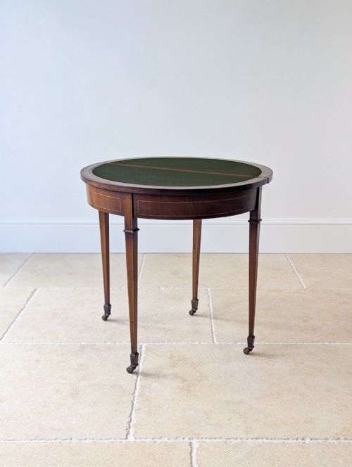 fig 1. An Edwardian mahogany demilune card table featuring inlaid stringing detail, square tapered legs, and small brass castors.