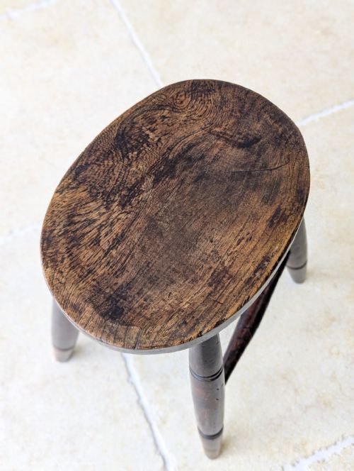 fig 1. An antique dark oak country stool with a thick circular seat, turned splayed legs, and cross stretchers.