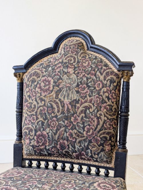fig 1. A low-seated Victorian Aesthetic Movement chair featuring ebonised turned wood detailing, a gallery of spindles, floral tapestry upholstery, and front brass castors.