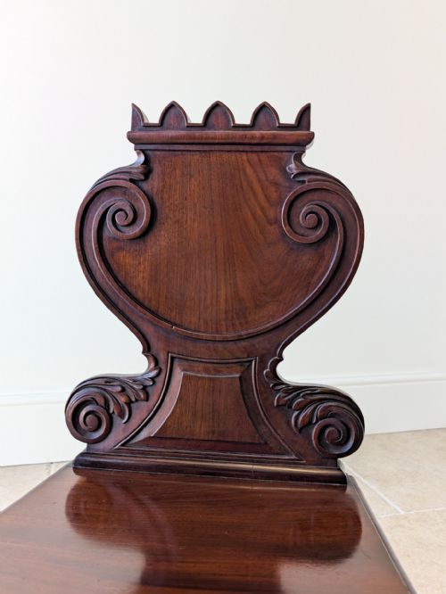 fig 1. A dark mahogany William IV hall chair featuring a carved scrollwork backrest with cresting and turned front legs.