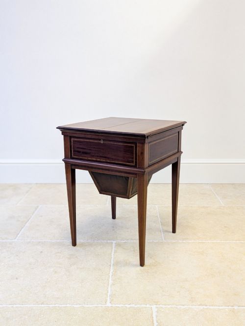 fig 1. An Edwardian mahogany metamorphic writing table featuring opened side leaves, an angled leather inset writing slope, and tapered legs with line inlay.