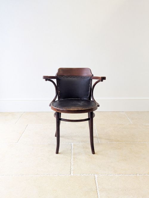 fig 1. An Edwardian dark brown bentwood desk chair featuring curved wooden armrests and a dark leather upholstered seat and backrest with brass stud detailing.