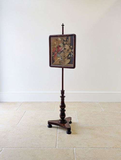 fig 2. A William IV rosewood pole screen featuring a square needlepoint panel displaying a parrot and flowers, set on a turned column with a triform base.