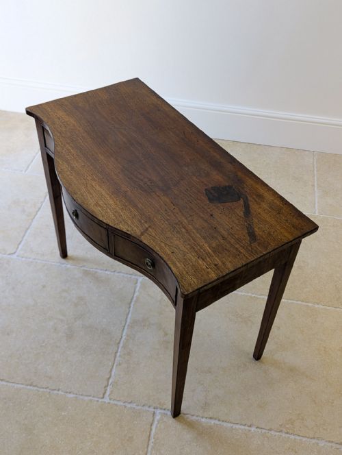 fig 1. A Georgian mahogany side table featuring a serpentine front profile, three drawer fronts with circular brass handles, and four tapered legs.
