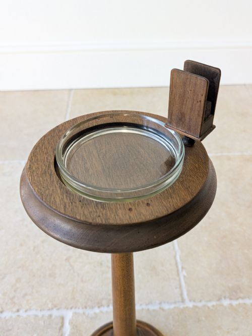 fig 1. An Edwardian mahogany floor-standing smoking stand featuring a turned central column, a circular stepped base, a glass tray insert, and a mounted timber matchbox holder.