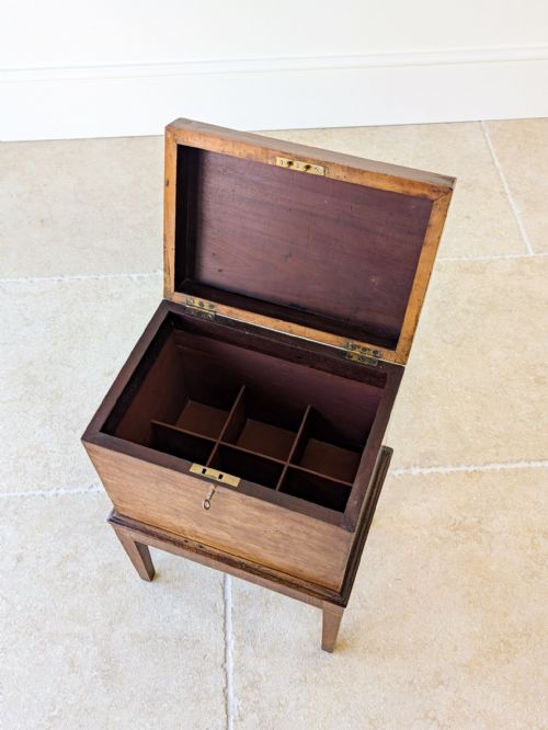 fig 1. An antique George III dark mahogany cellaret chest featuring a hinged top, inlaid escutcheon, and square tapered legs on a stone tile floor.