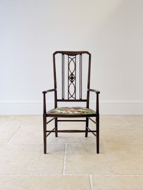 fig 1. An Edwardian mahogany elbow chair with an inlaid pierced back splat, swept arms, and a floral needlepoint seat.