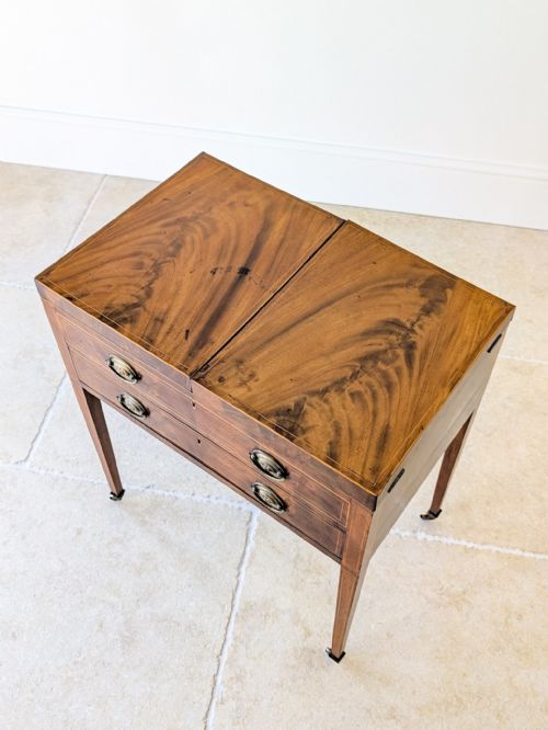 fig 1. An antique Georgian mahogany folding dressing table with fold-out side tops, a central pop-up mirror, brass handles, and square tapered legs on castors.