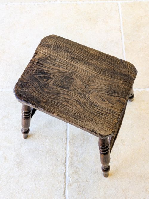 fig 1. A dark brown antique Victorian country stool made of elm and beech with turned wooden legs and a solid rectangular top.