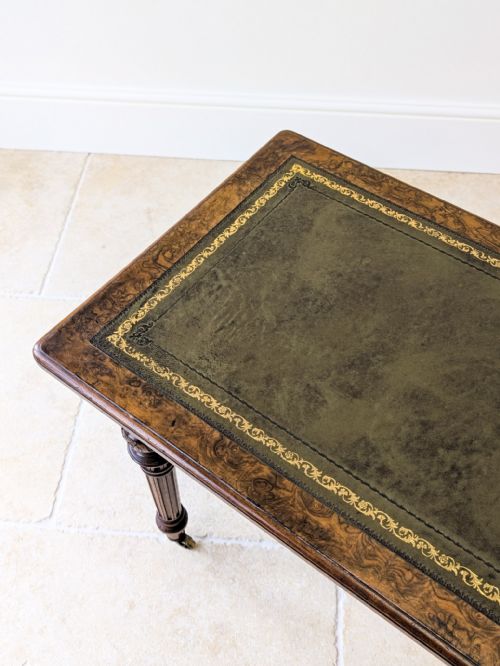 fig 1. A Victorian burr walnut writing table featuring a green leather inset top, fluted turned legs, carved detailing, and brass castors.