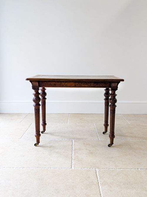 fig 2. A Victorian burr walnut writing table featuring a green leather inset top, fluted turned legs, carved detailing, and brass castors.