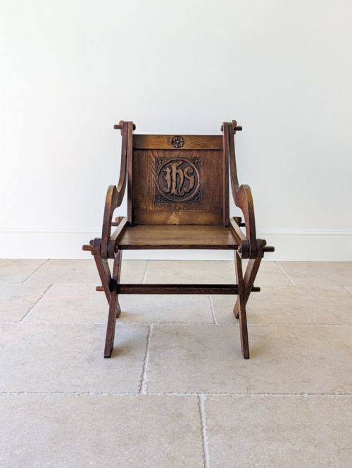 fig 1. An Edwardian dark oak Glastonbury armchair featuring an X-frame base, wooden peg construction, and a carved IHS monogram back panel.