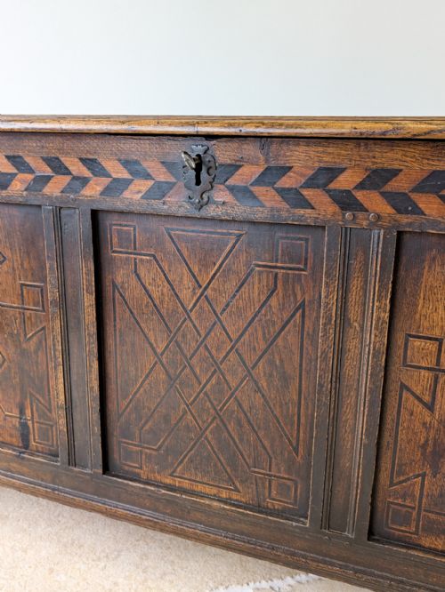 fig 1. A 17th-century Charles II dark oak coffer featuring a geometric inlaid frieze and three carved geometric front panels.