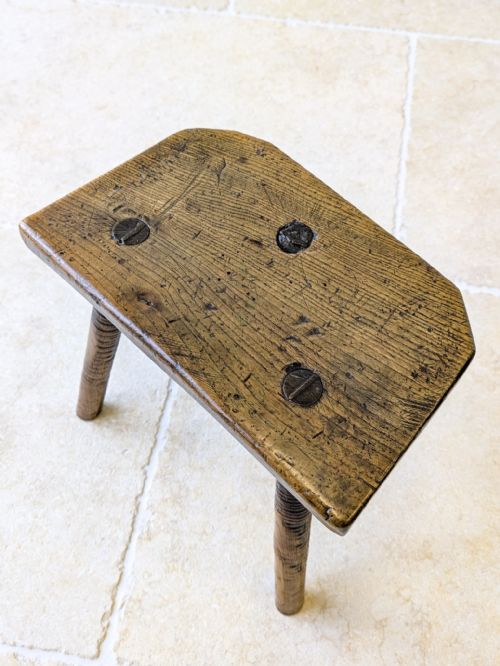 fig 1. A rustic nineteenth-century dark wood three-legged stool with a contoured elm seat and turned ash splayed legs.