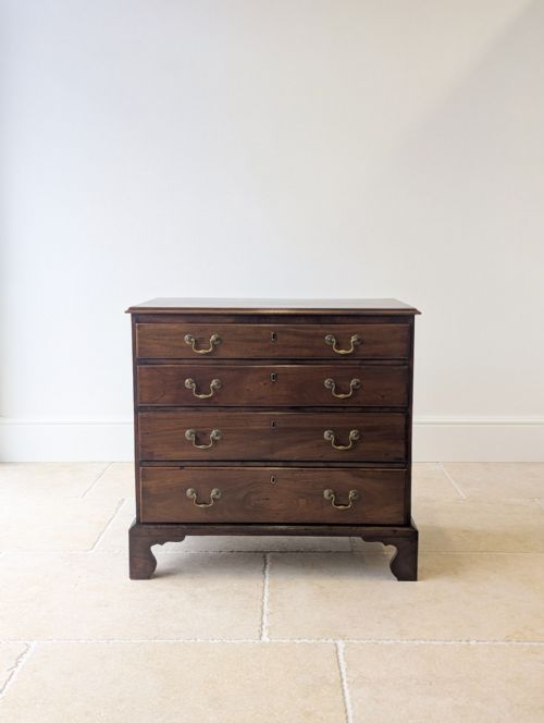 fig 1. An 18th-century George III mahogany chest of drawers featuring four graduated drawers with brass swan-neck handles, supported on shaped bracket feet.