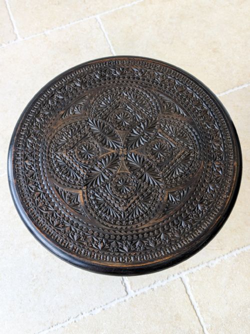 fig 1. An antique Victorian ebonised wooden occasional table with an intricately hand-carved circular top, a turned central stem, and a carved tripod base.