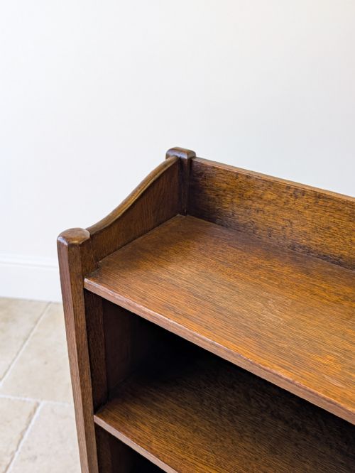 fig 1. A tall, narrow dark oak Arts and Crafts open bookcase featuring four fixed shelves and shaped side galleries.