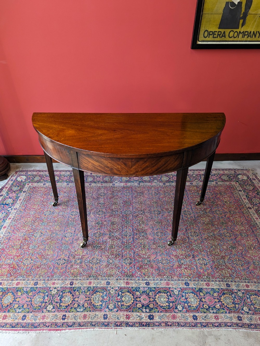 A freestanding antique Victorian mahogany demilune table featuring a curved top, tapered legs with castors, and rich grain patterns. View II