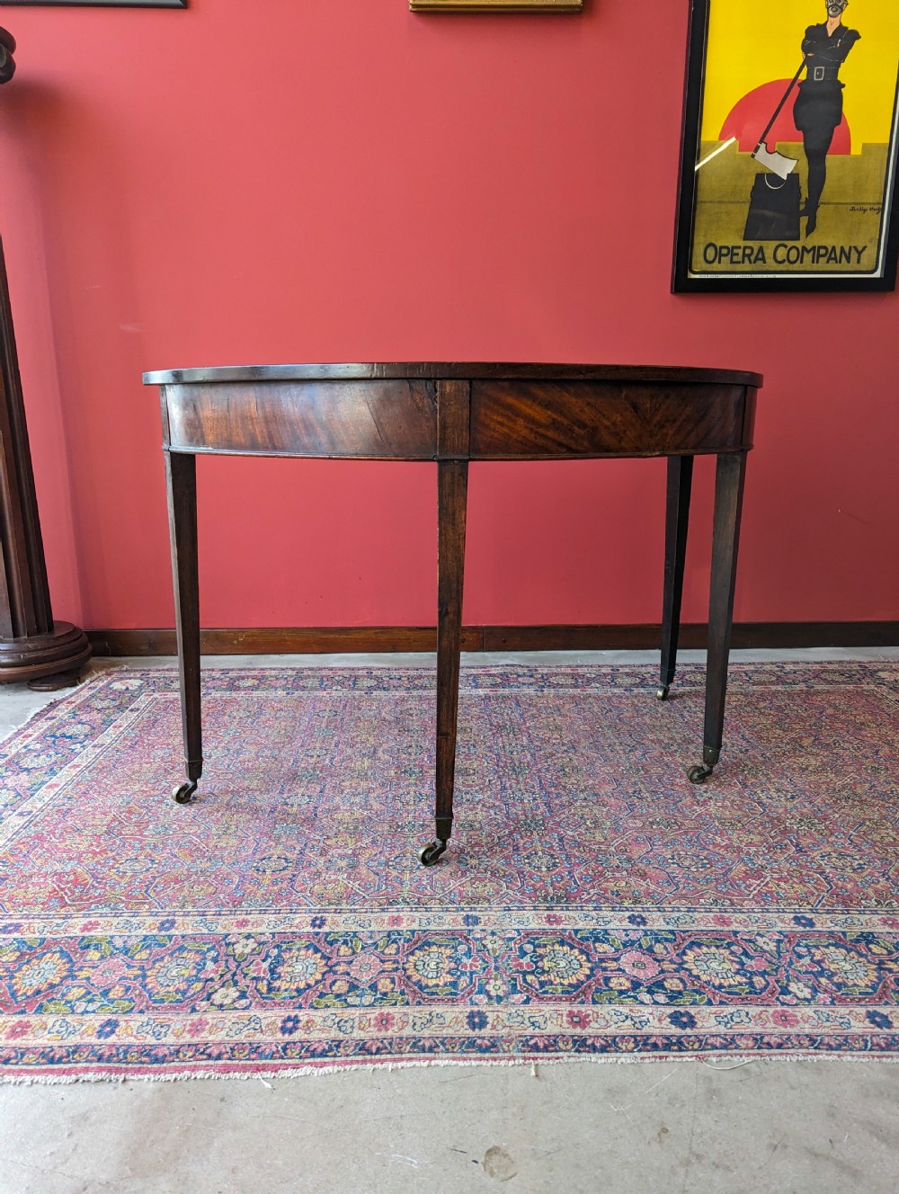 A freestanding antique Victorian mahogany demilune table featuring a curved top, tapered legs with castors, and rich grain patterns. View III