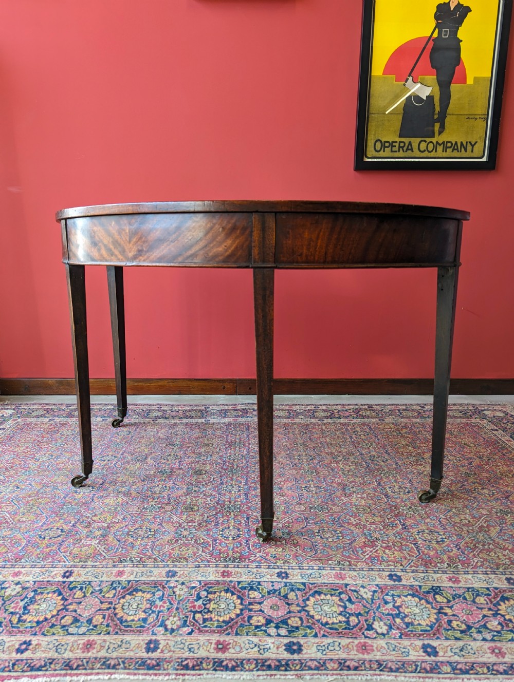 A freestanding antique Victorian mahogany demilune table featuring a curved top, tapered legs with castors, and rich grain patterns. View IV