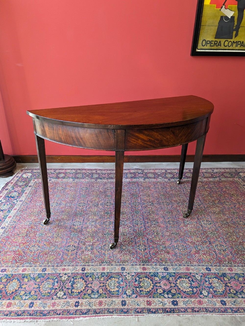 A freestanding antique Victorian mahogany demilune table featuring a curved top, tapered legs with castors, and rich grain patterns. View VII