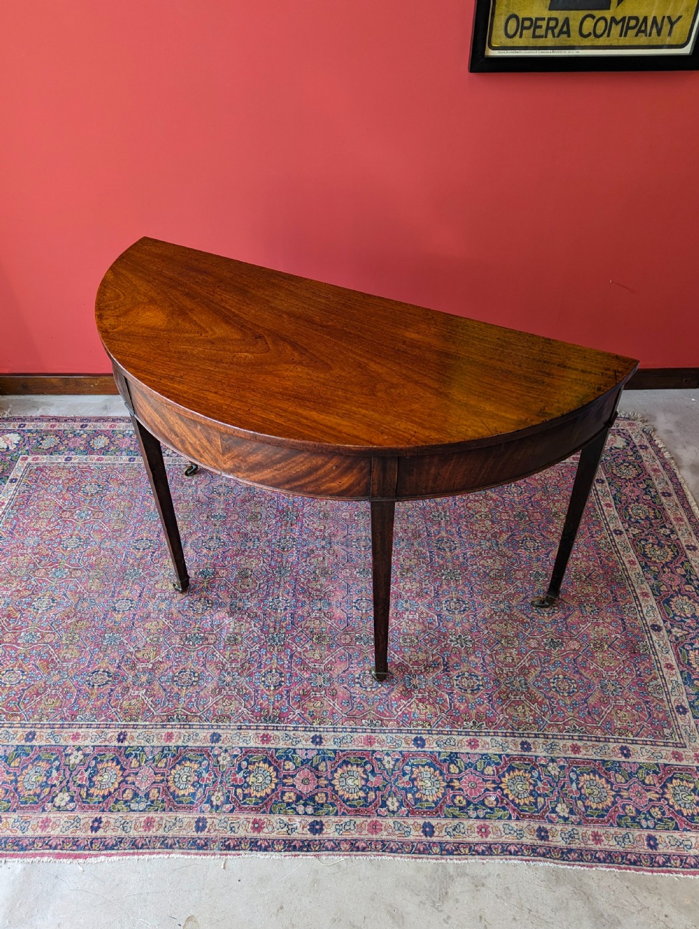 A freestanding antique Victorian mahogany demilune table featuring a curved top, tapered legs with castors, and rich grain patterns. View IX