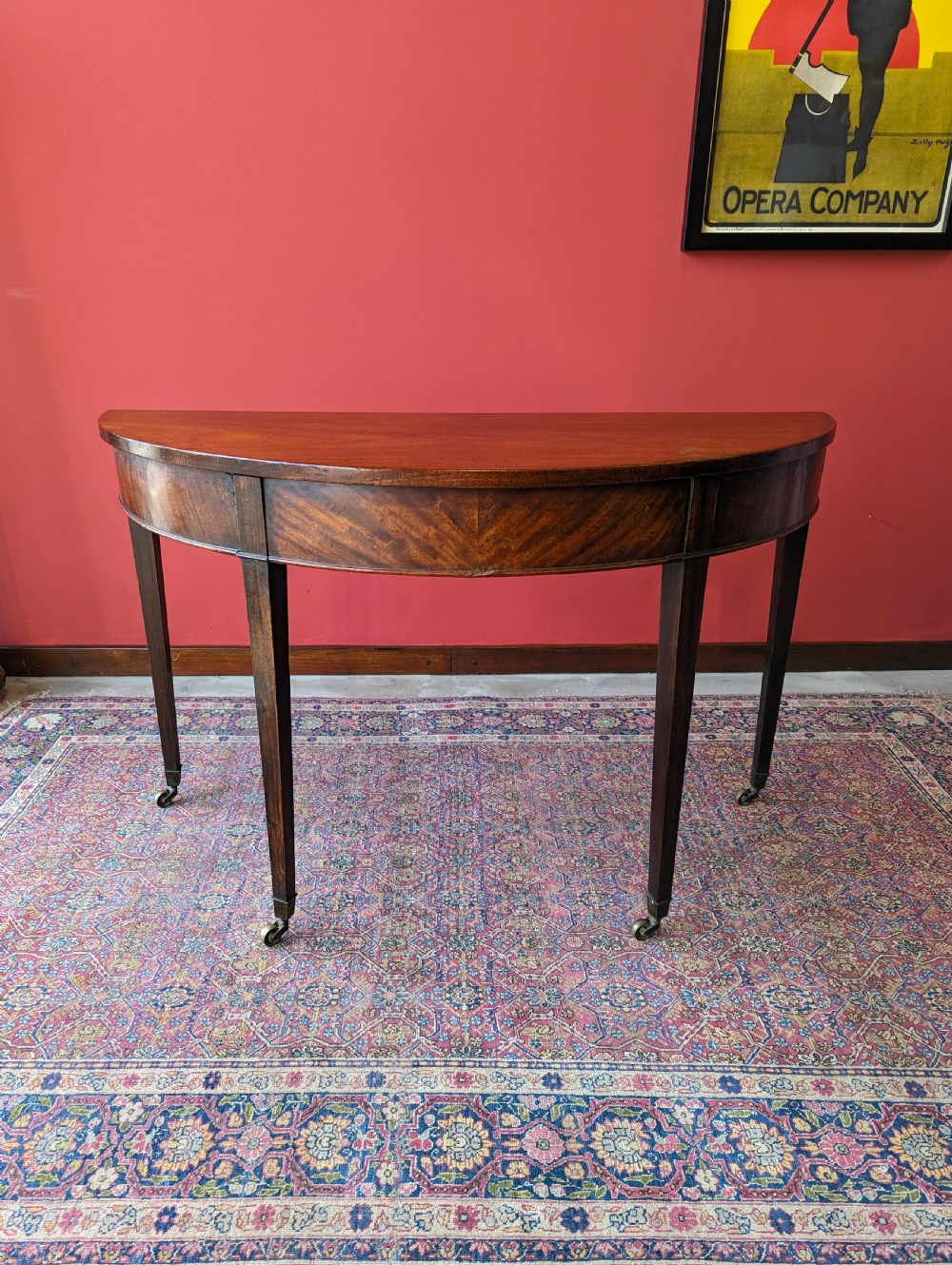 A freestanding antique Victorian mahogany demilune table featuring a curved top, tapered legs with castors, and rich grain patterns. View X