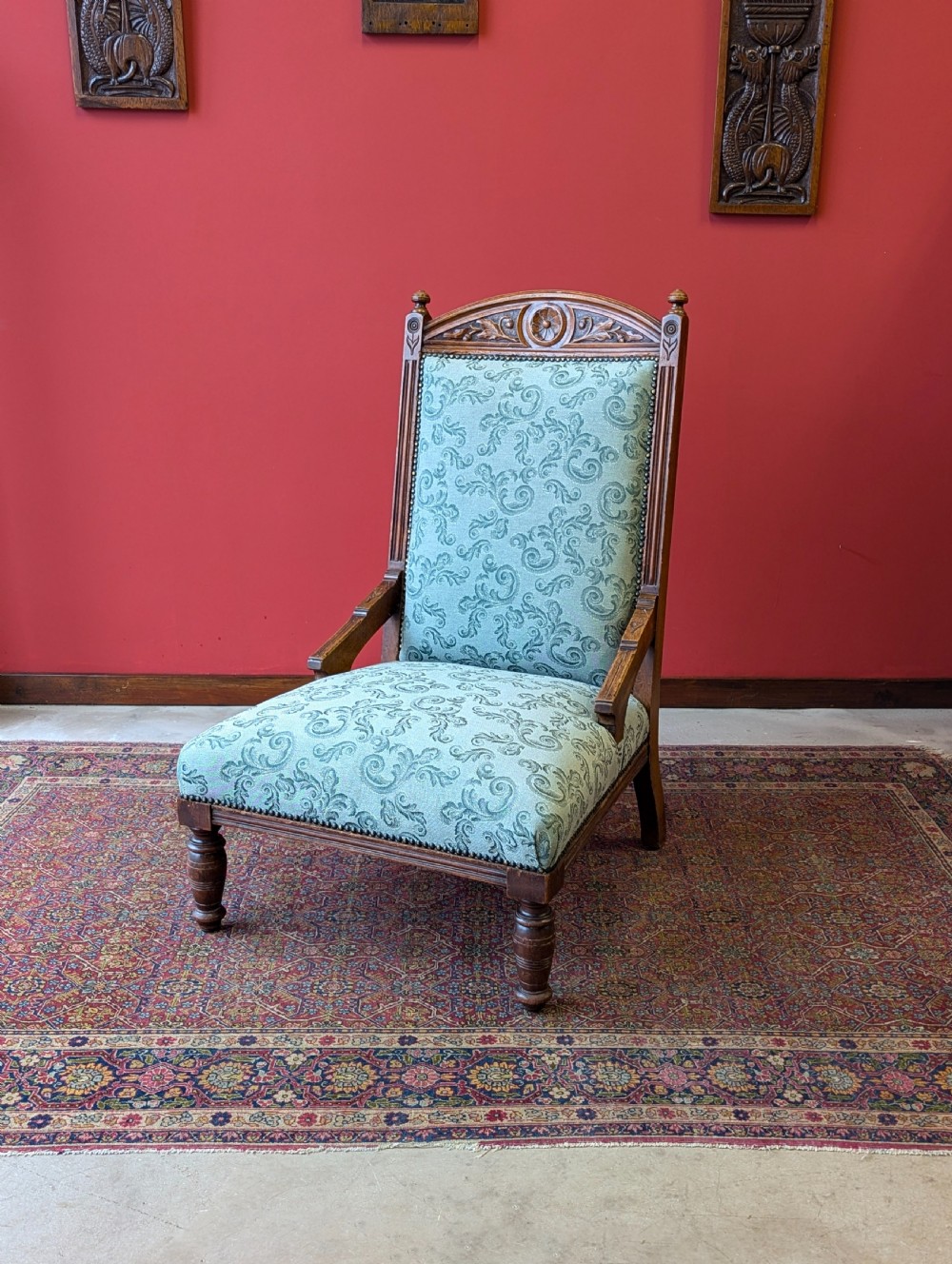 An antique Victorian mahogany easy chair upholstered in patterned teal fabric with carved wooden details and turned front legs.