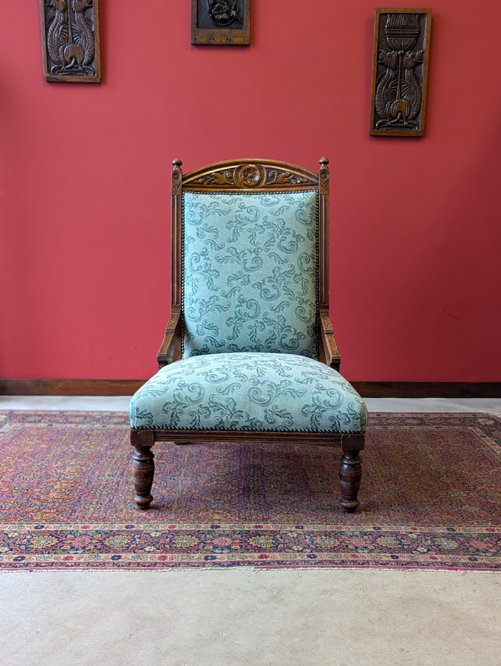An antique Victorian mahogany easy chair upholstered in patterned teal fabric with carved wooden details and turned front legs. View II