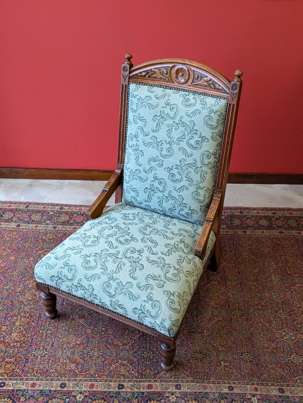 An antique Victorian mahogany easy chair upholstered in patterned teal fabric with carved wooden details and turned front legs. View VII