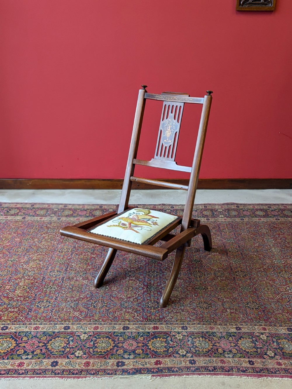 An antique Edwardian folding campaign chair made of mahogany featuring marquetry inlay and an upholstered seat pad.