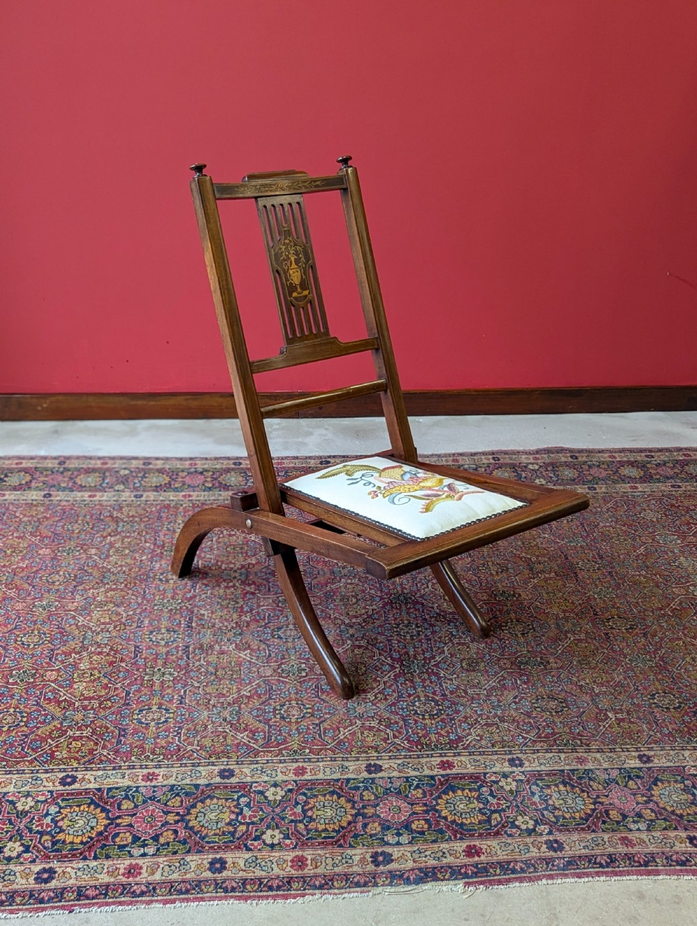 An antique Edwardian folding campaign chair made of mahogany featuring marquetry inlay and an upholstered seat pad. View IX