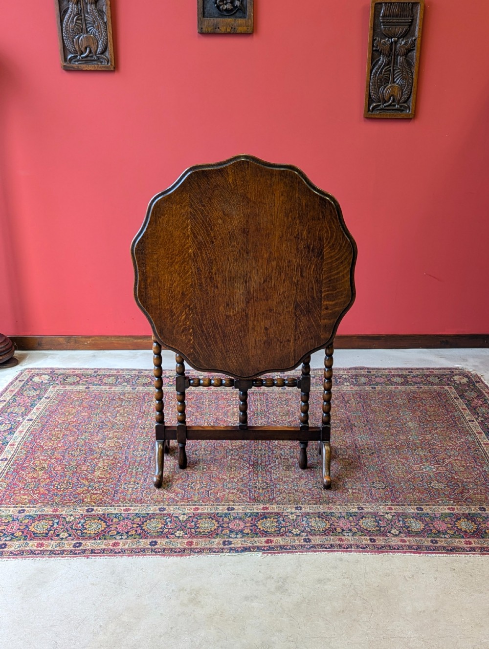 An antique early 20th-century oak folding table featuring a shaped top and turned bobbin legs, shown folded upright.