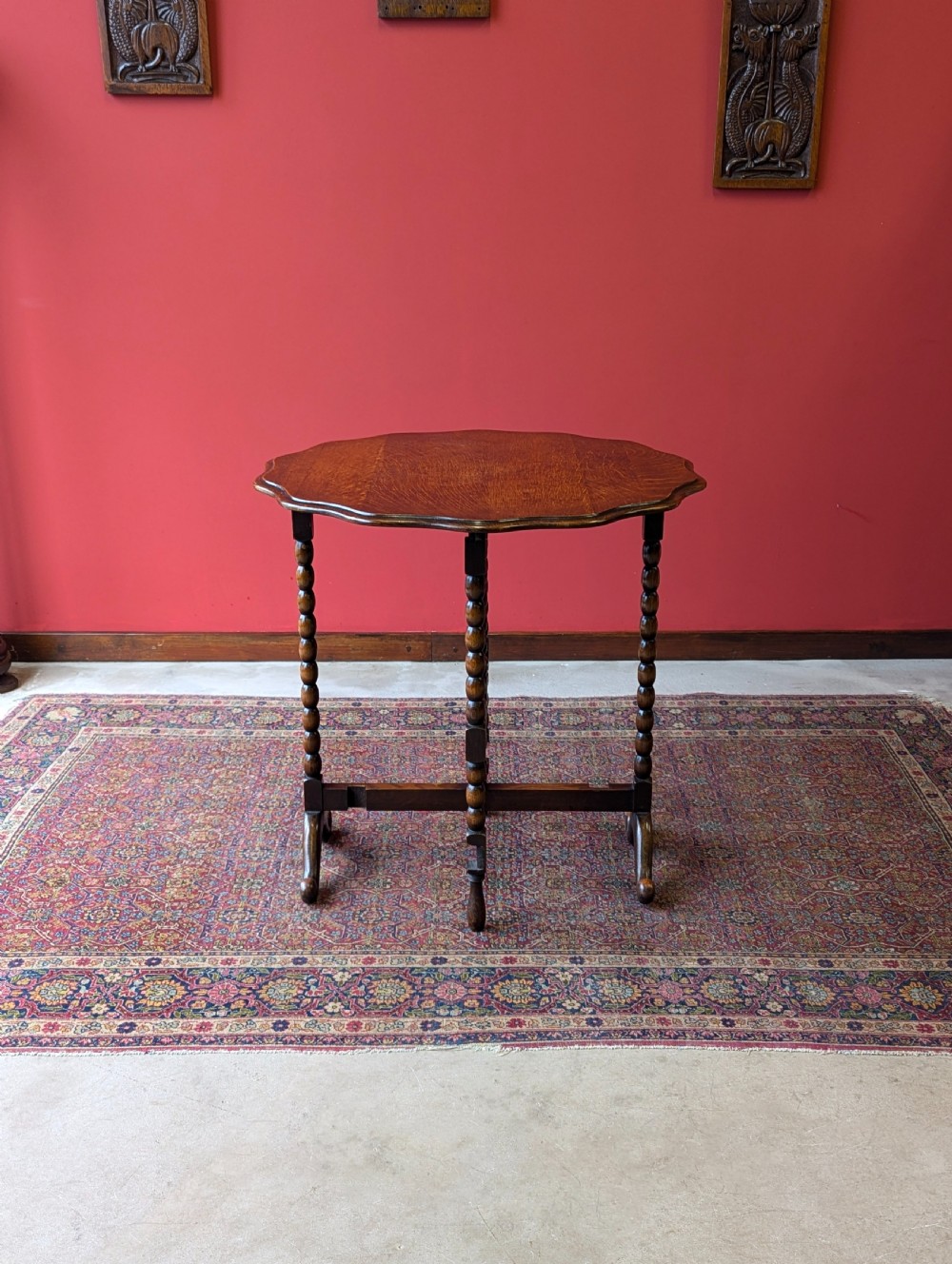 An antique early 20th-century oak folding table featuring a shaped top and turned bobbin legs, shown folded upright. View II