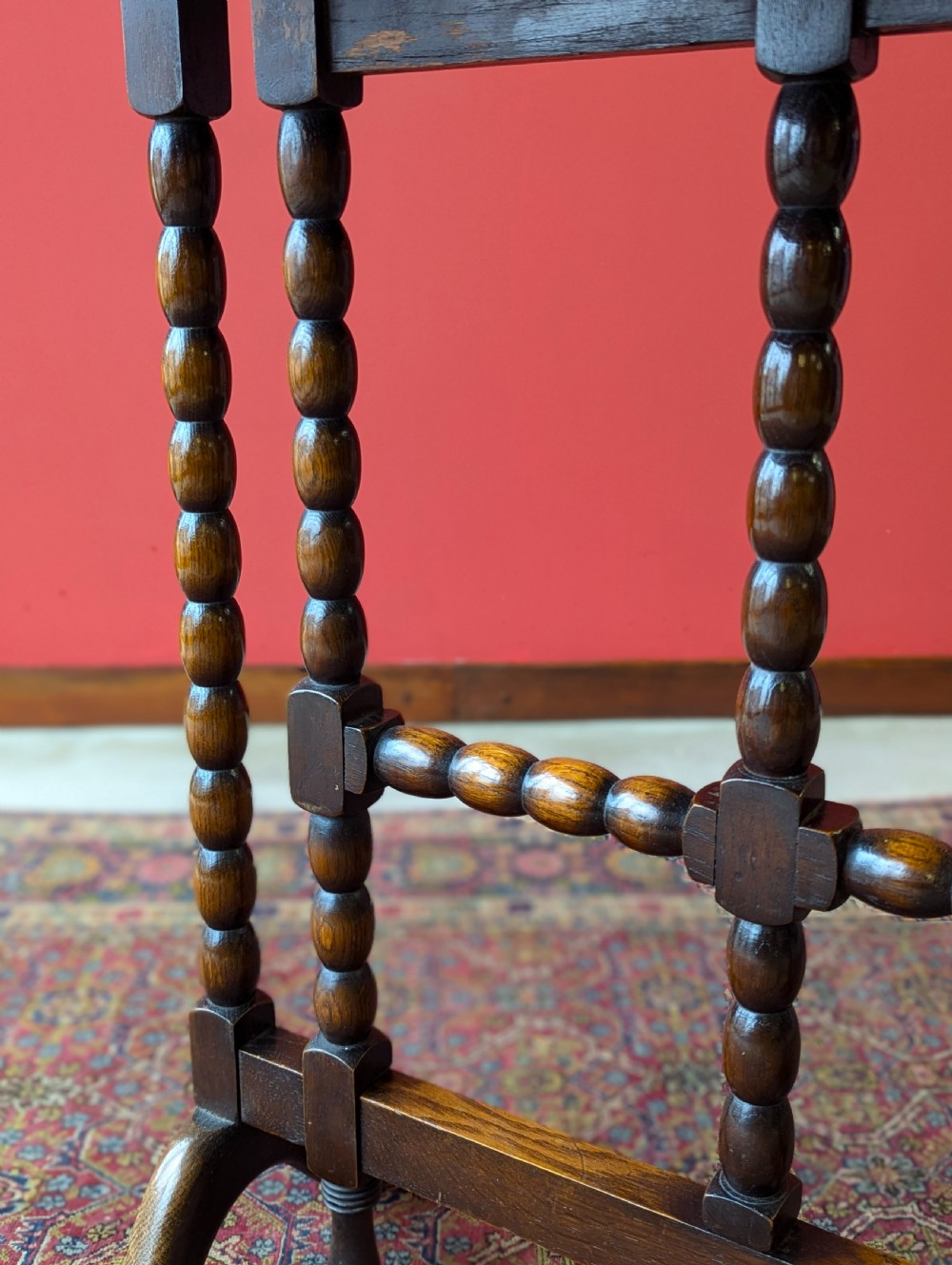 An antique early 20th-century oak folding table featuring a shaped top and turned bobbin legs, shown folded upright. View III