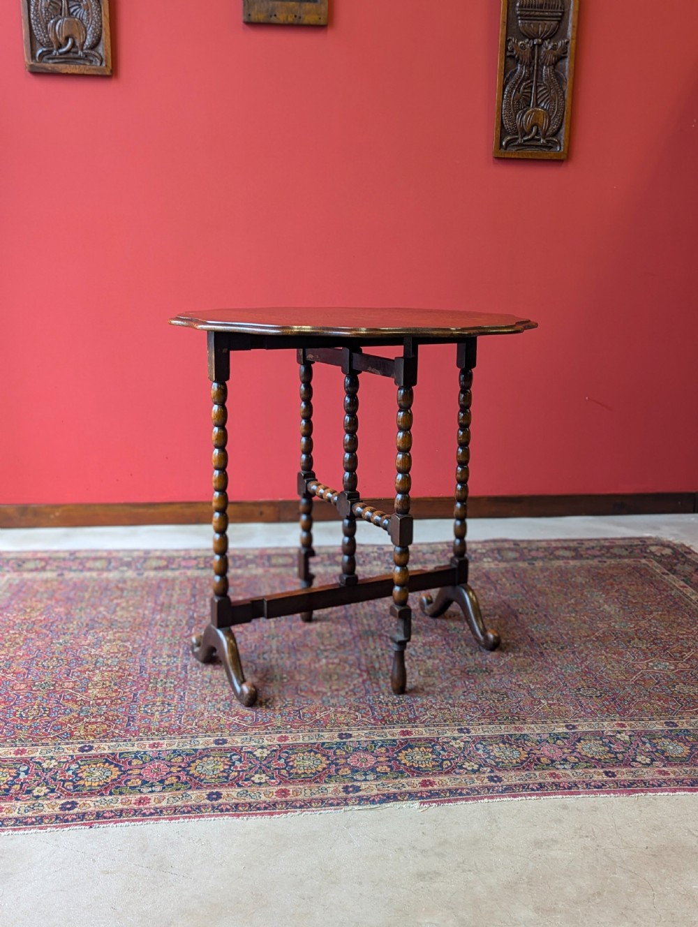 An antique early 20th-century oak folding table featuring a shaped top and turned bobbin legs, shown folded upright. View V