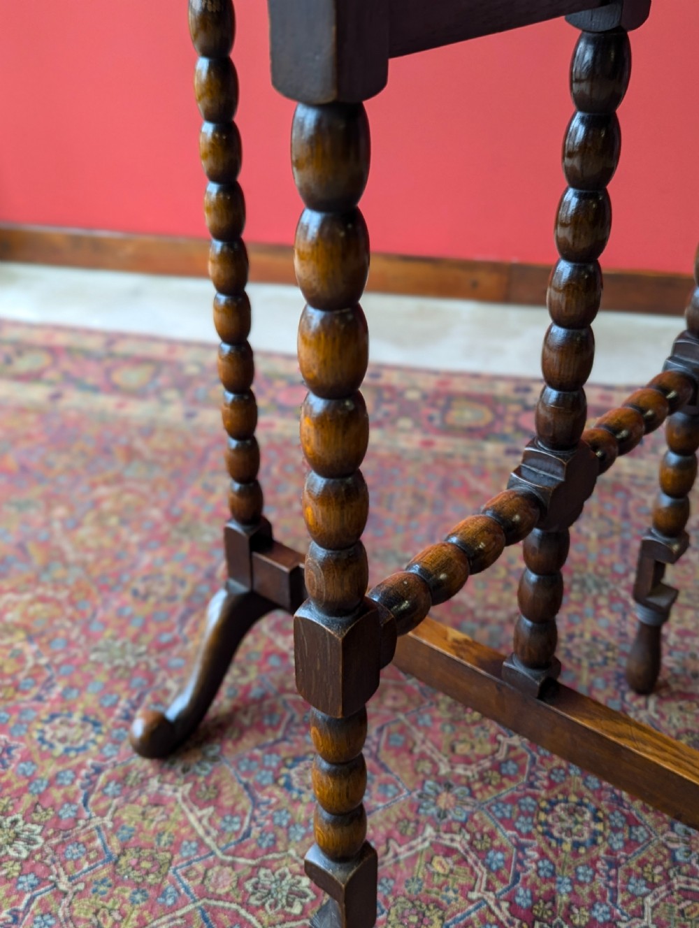An antique early 20th-century oak folding table featuring a shaped top and turned bobbin legs, shown folded upright. View VI