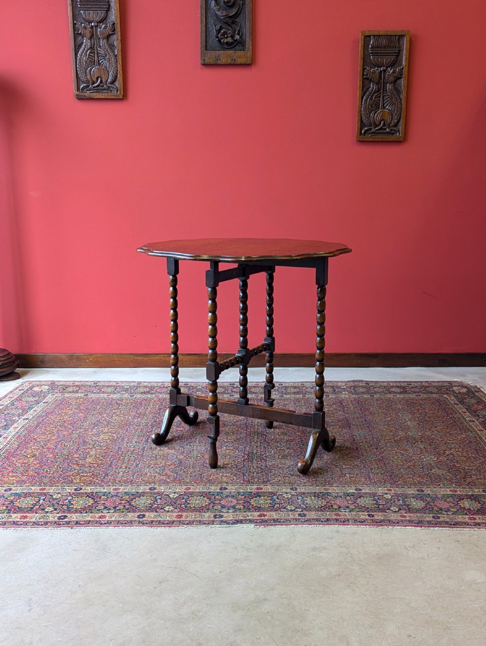 An antique early 20th-century oak folding table featuring a shaped top and turned bobbin legs, shown folded upright. View VII
