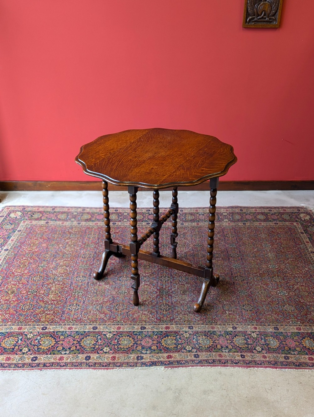 An antique early 20th-century oak folding table featuring a shaped top and turned bobbin legs, shown folded upright. View VIII