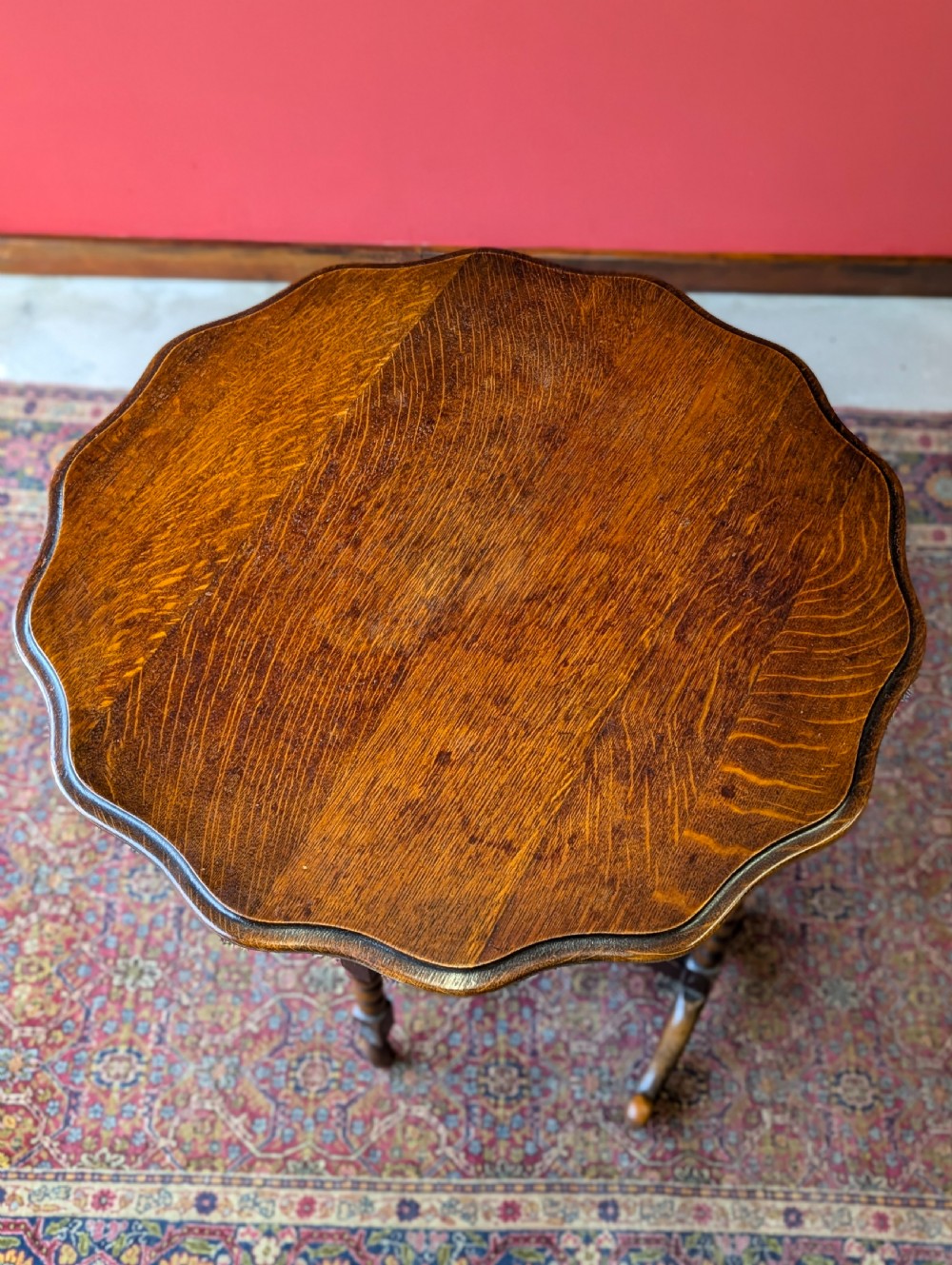 An antique early 20th-century oak folding table featuring a shaped top and turned bobbin legs, shown folded upright. View IX