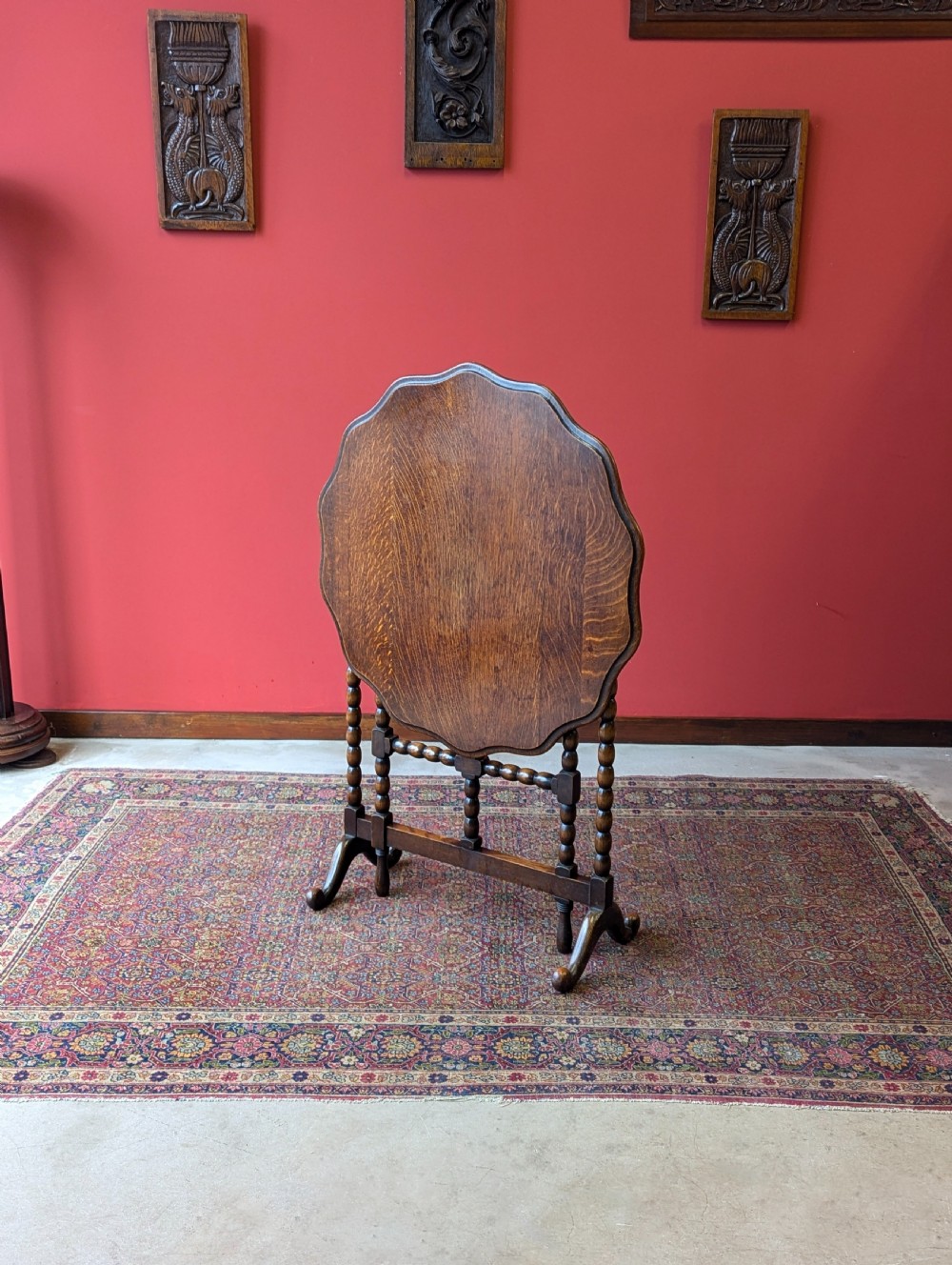 An antique early 20th-century oak folding table featuring a shaped top and turned bobbin legs, shown folded upright. View X
