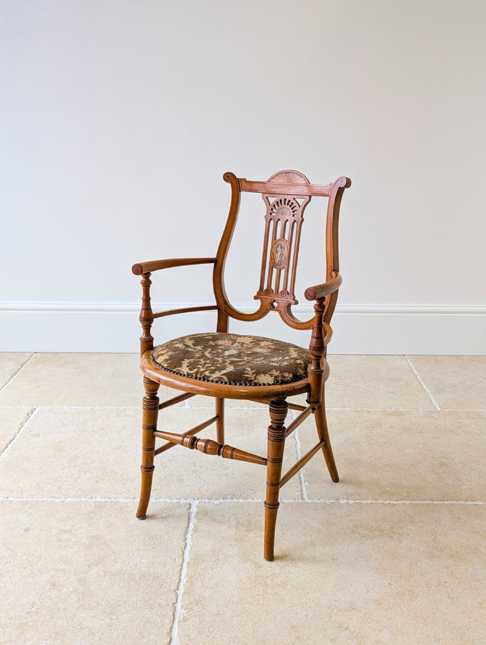 A late Victorian satinwood elbow chair featuring a lyre-shaped backrest with a painted central medallion, turned front legs, and an upholstered seat.