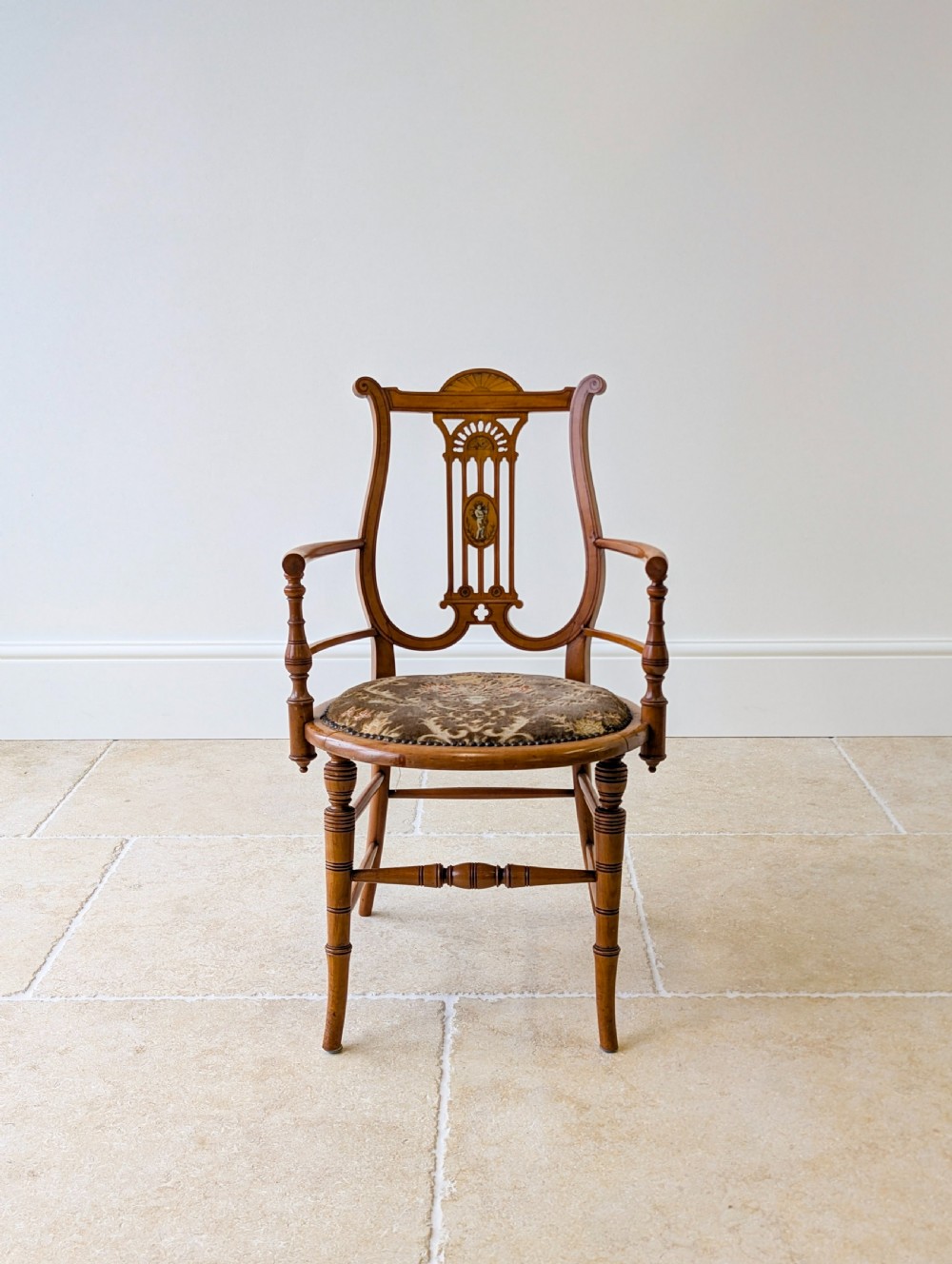 A late Victorian satinwood elbow chair featuring a lyre-shaped backrest with a painted central medallion, turned front legs, and an upholstered seat. View II