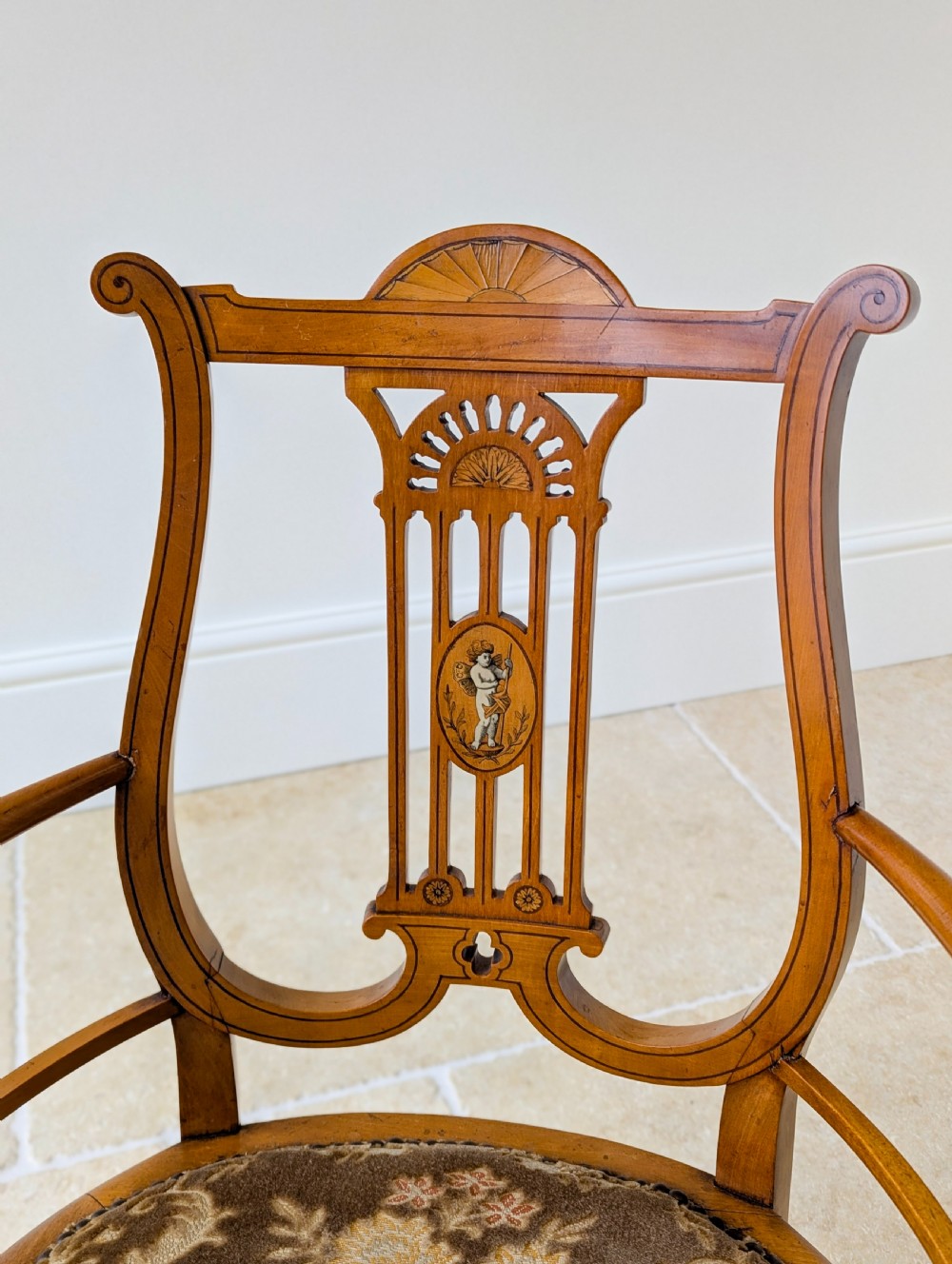 A late Victorian satinwood elbow chair featuring a lyre-shaped backrest with a painted central medallion, turned front legs, and an upholstered seat. View III