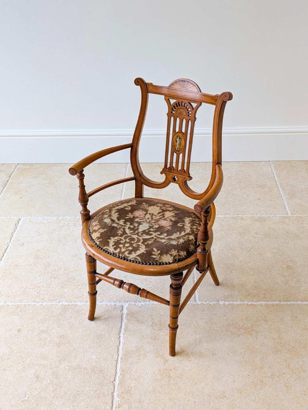 A late Victorian satinwood elbow chair featuring a lyre-shaped backrest with a painted central medallion, turned front legs, and an upholstered seat. View VII