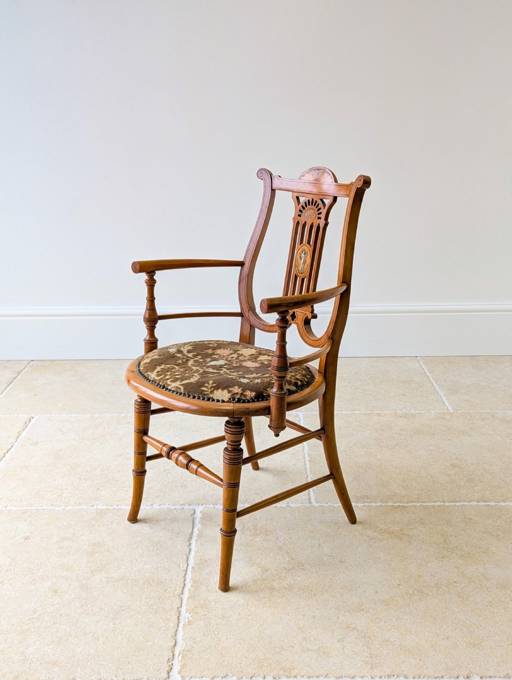 A late Victorian satinwood elbow chair featuring a lyre-shaped backrest with a painted central medallion, turned front legs, and an upholstered seat. View IX