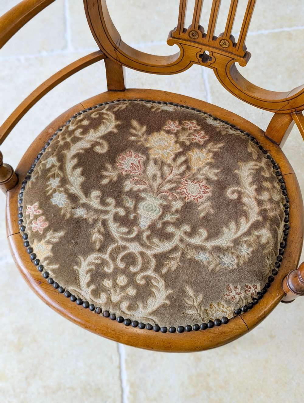 A late Victorian satinwood elbow chair featuring a lyre-shaped backrest with a painted central medallion, turned front legs, and an upholstered seat. View X