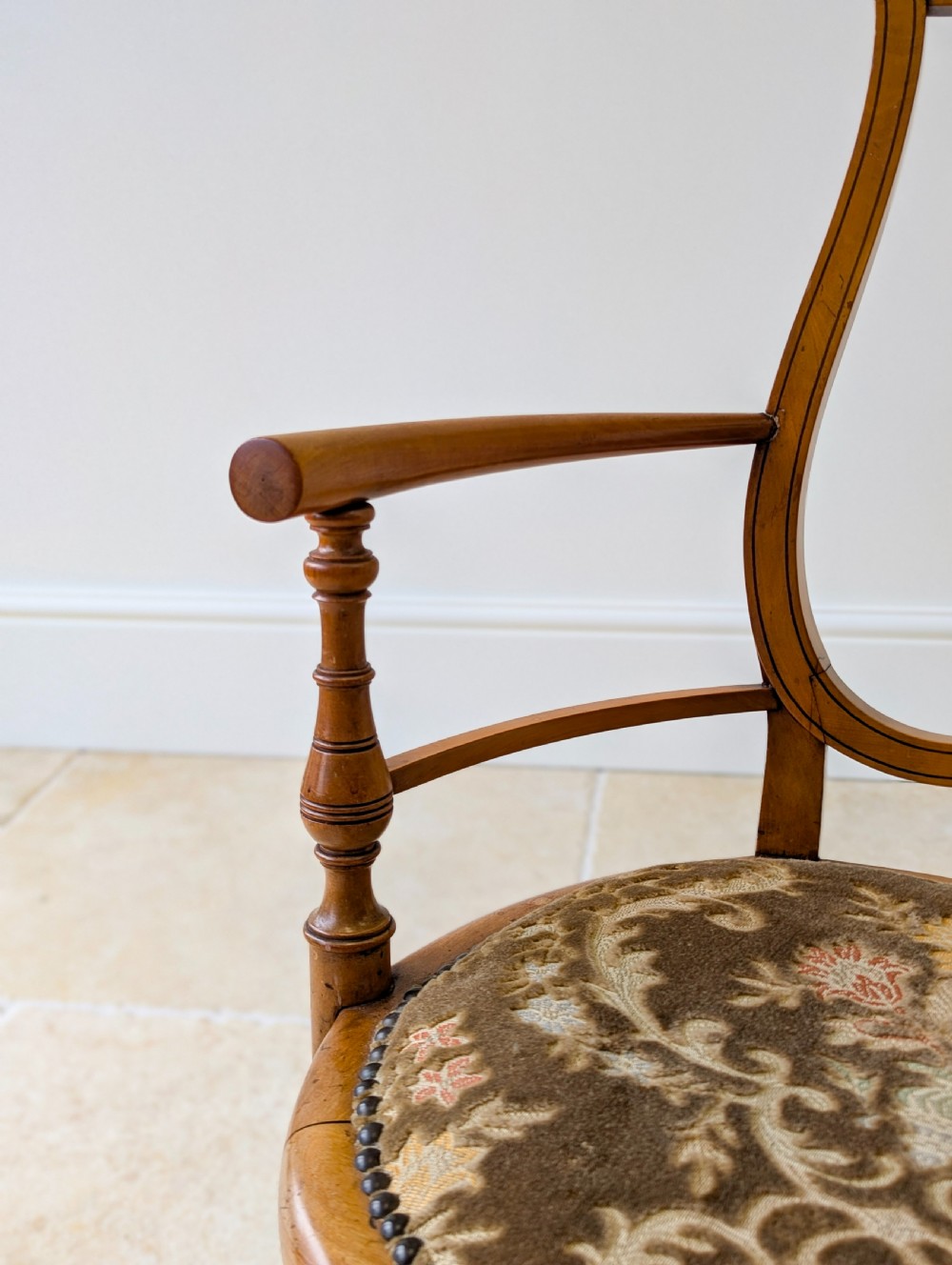 A late Victorian satinwood elbow chair featuring a lyre-shaped backrest with a painted central medallion, turned front legs, and an upholstered seat. View XII